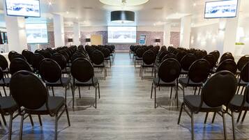 Un salón de conferencias con filas de sillas, una lámpara grande en el techo y una pantalla al frente.