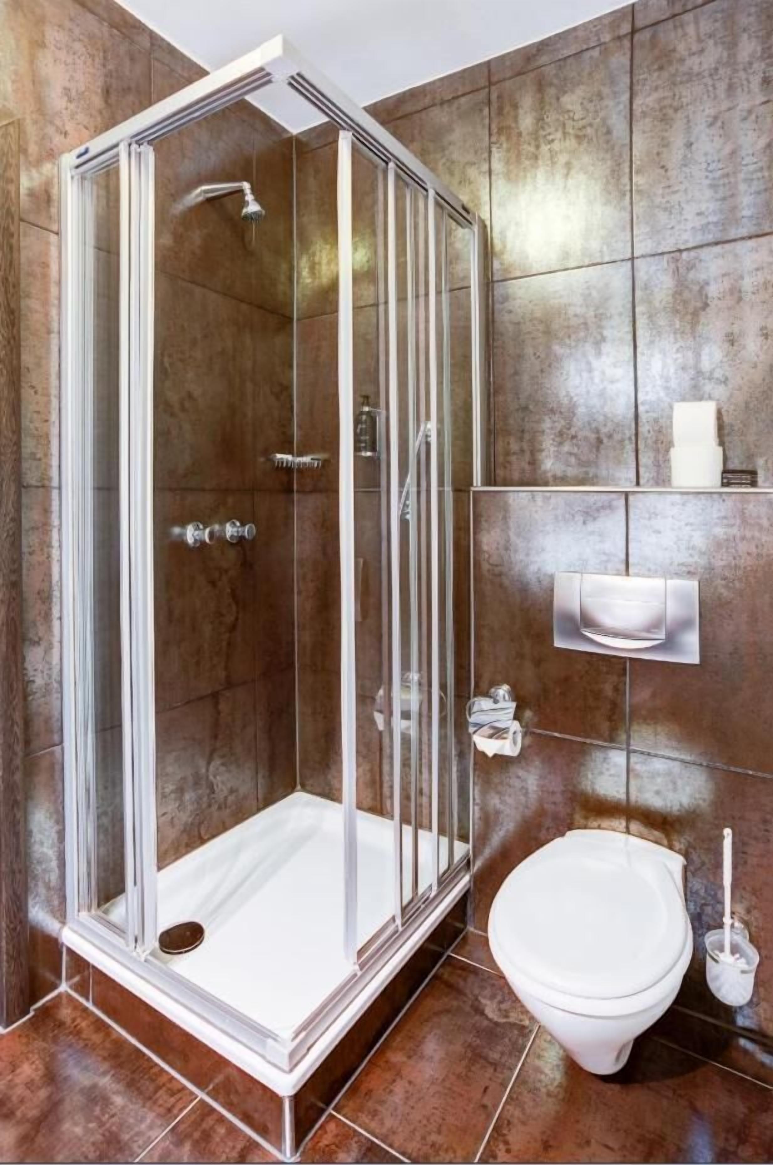 A modern bathroom with a glass-enclosed shower, a white toilet, and a marble-tiled wall.