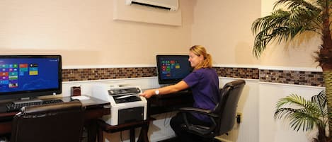 Una mujer trabajando en un escritorio con dos monitores, una impresora y un teclado.