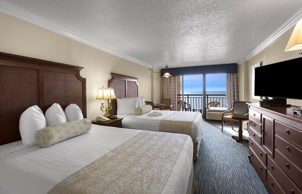 A hotel room with two beds, a television, a desk, and a view of the ocean.