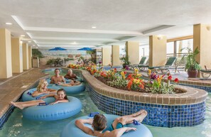 An indoor swimming pool with blue water slides, lounge chairs, and potted plants. - Holiday Pavilion Resort on the Boardwalk (Myrtle Beach)