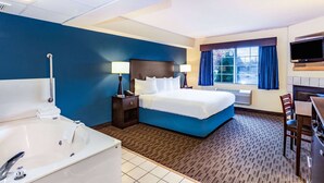 Quarto de hotel com uma cama grande, banheiro privativo com banheira, uma escrivaninha e televisão.