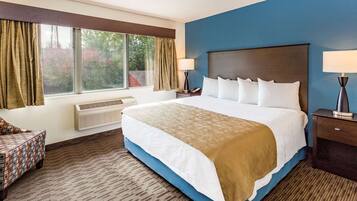 A hotel room with a large bed, two bedside tables with lamps, a window with curtains, and a patterned chair.