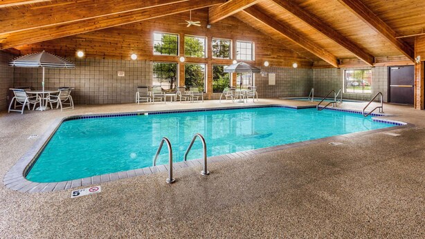 Uma piscina interior com teto de madeira, janelas amplas e chão ladrilhado.