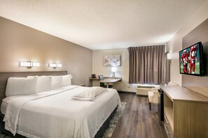 A hotel room with a large bed, a desk, a chair, a television, and a window with curtains. - Red Roof Inn PLUS+ Boston - Logan (Saugus)