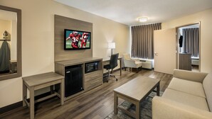 A hotel room with a flat-screen TV mounted on the wall, a small kitchenette with a refrigerator and microwave, a sofa, a coffee table, and a desk with a chair. - Red Roof Inn PLUS+ Boston - Logan (Saugus)