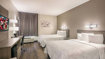 A hotel room with two beds, a desk, a chair, a flat-screen TV, and a window with curtains.