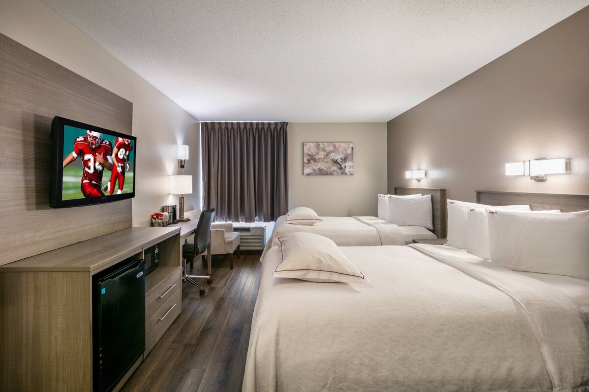 A hotel room with a TV, two beds, a desk, and a chair.