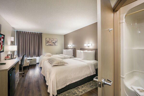 Une chambre d’hôtel comprenant un lit, des tables de chevet, un bureau avec une chaise, une télévision et une salle de bain avec une baignoire.