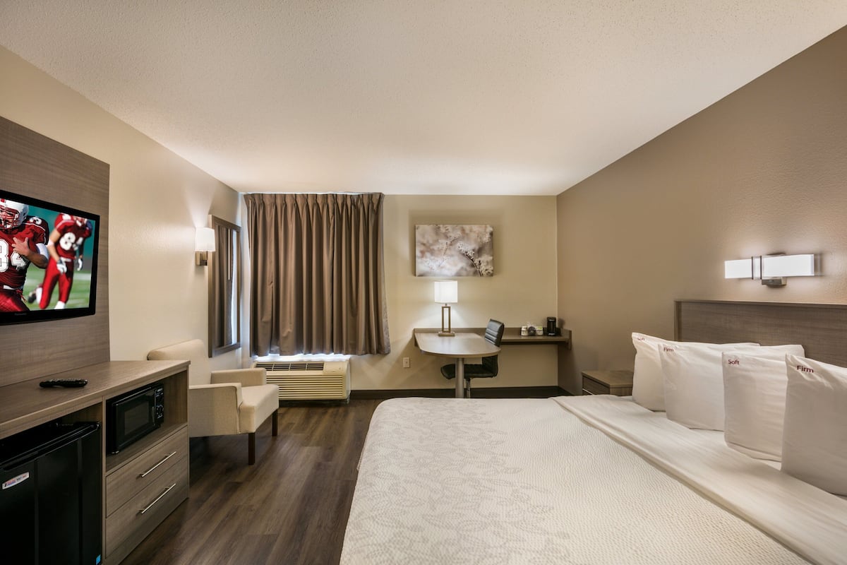 A hotel room with a bed, a desk, a TV, a microwave, and a window with curtains.