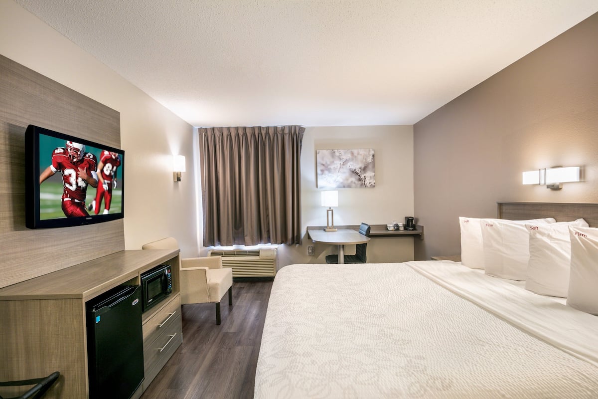 A hotel room with a bed, a desk, a chair, a television, a lamp, and a painting on the wall.