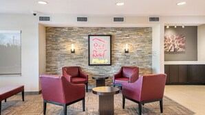 A lobby area with two red leather chairs, a small round table, a stone wall with a neon sign, and a framed picture. - Red Roof Inn PLUS+ Boston - Logan (Saugus)