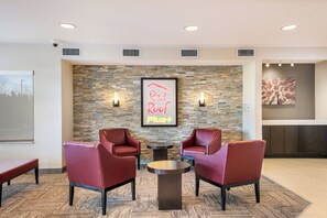 A lobby area with two red leather chairs, a small round table, a stone wall with a neon sign, and a framed picture.