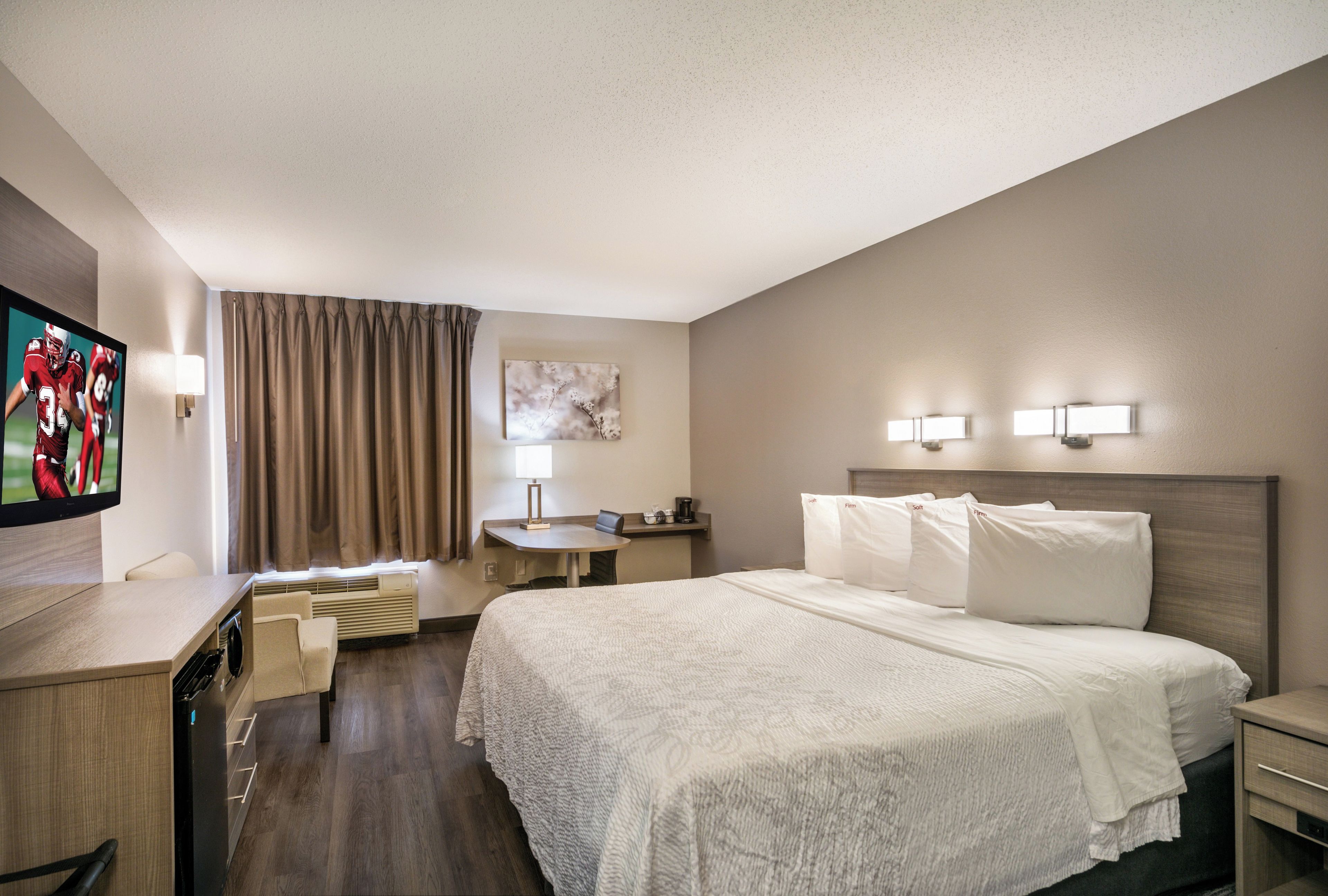 A hotel room with a bed, a desk, a television, and a window with curtains.