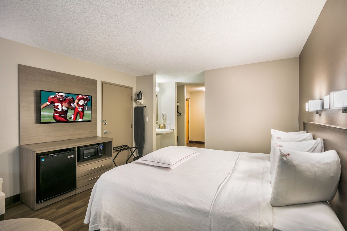A hotel room with a bed, a TV mounted on the wall, a microwave, and a refrigerator.