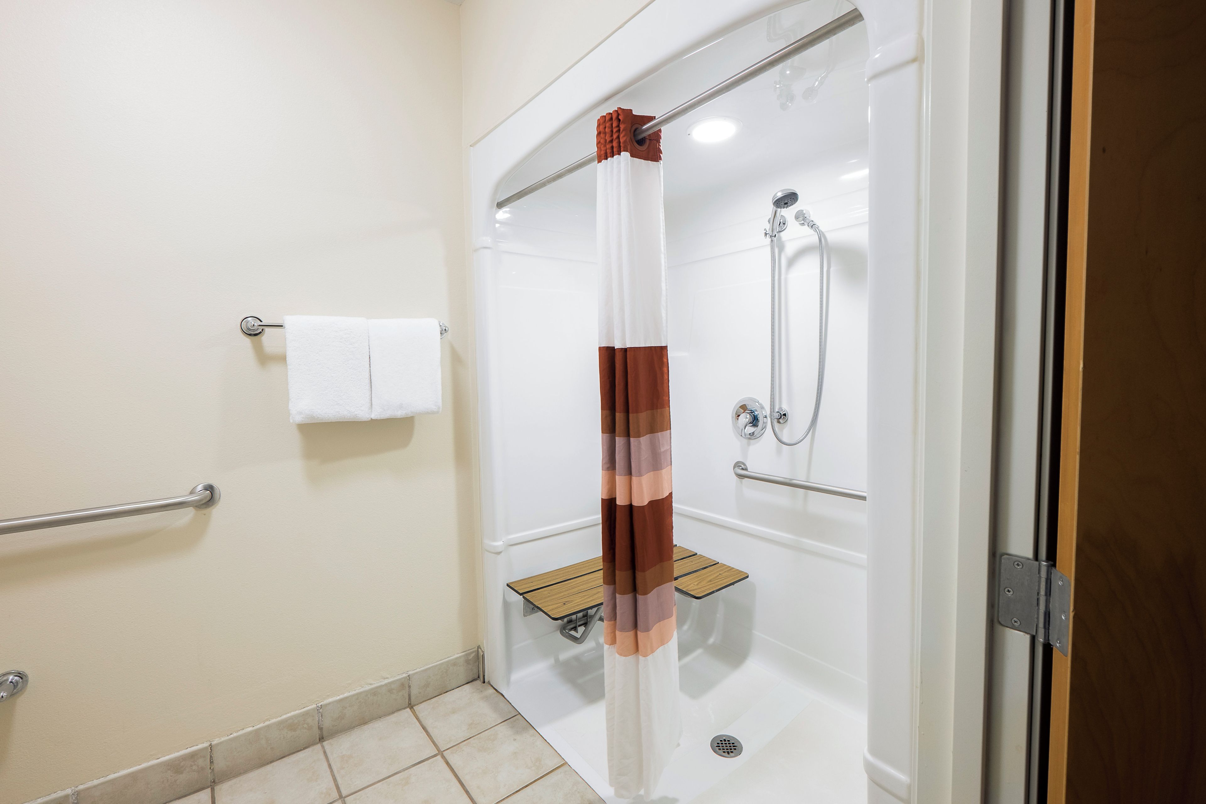 Een moderne badkamer met een douche in een glazen cabine, een witte handdoek op een rek en een houten plank.