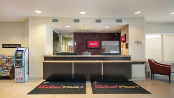 A hotel reception area with a Red Roof Plus+ sign, an ATM, and a sign indicating free Wi-Fi in all rooms.