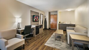 A hotel room with a flat-screen TV mounted on the wall, a desk with a chair, a sofa, a small table, and a kitchenette area. - Red Roof Inn PLUS+ Boston - Logan (Saugus)