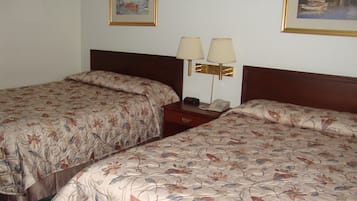 A hotel room with two single beds, each with floral-patterned bedding, a wooden headboard, and a nightstand with a lamp and a telephone.