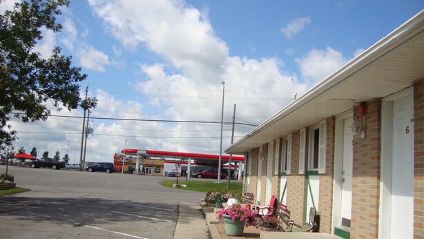 Un motel con una gasolinera al fondo, un estacionamiento y una acera con plantas en macetas.