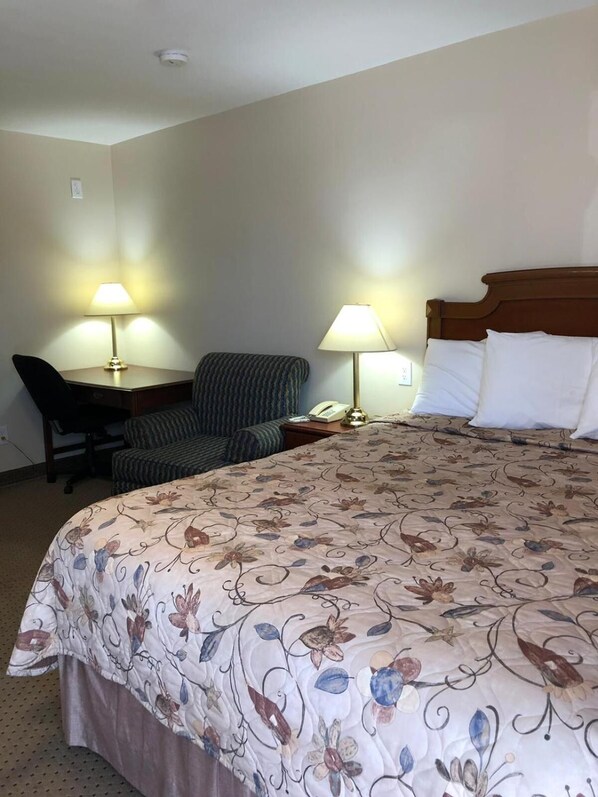 Una habitación de hotel con una cama grande, un escritorio con una silla, dos lámparas de noche y un teléfono sobre el escritorio.
