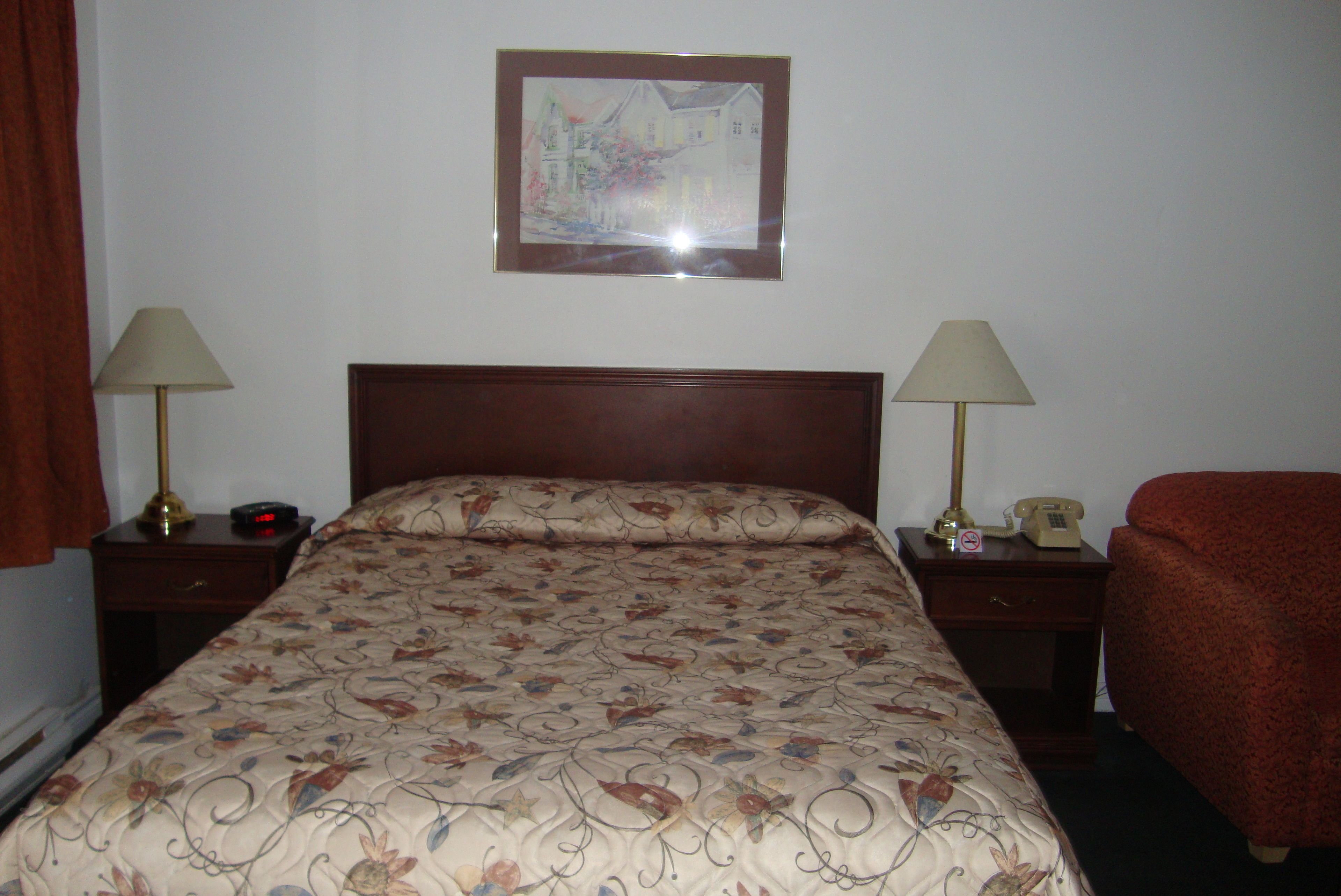 Habitación de hotel con una cama, dos mesitas de noche con lámparas, un teléfono y un cuadro en la pared.
