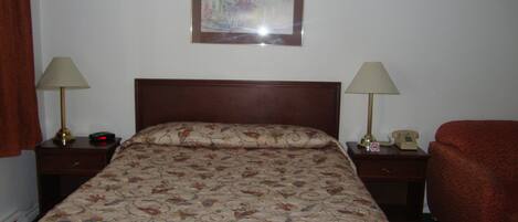 Habitación de hotel con una cama, dos mesitas de noche con lámparas, un teléfono y un cuadro en la pared.