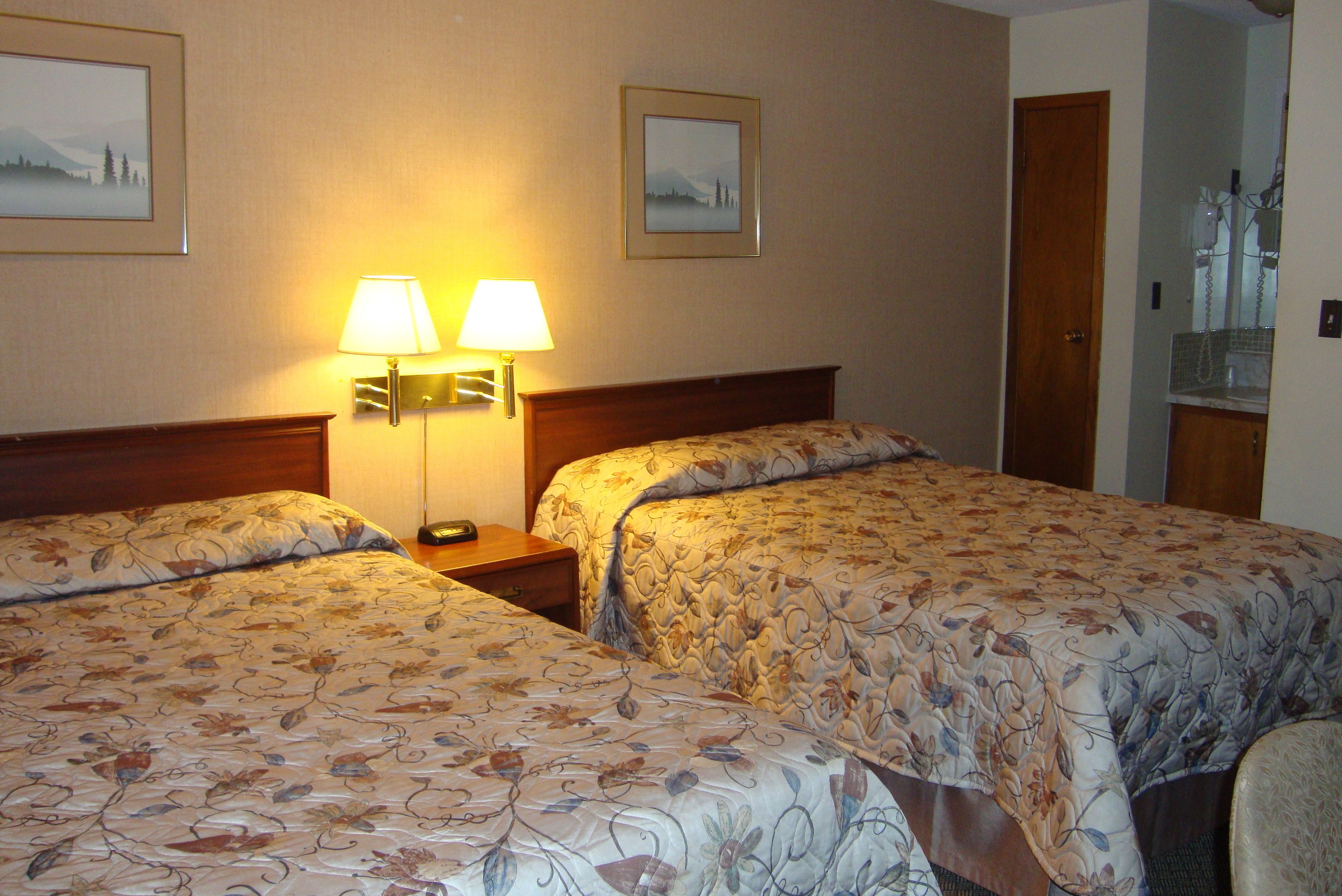 A hotel room with two beds, a nightstand with lamps, and framed pictures on the wall.
