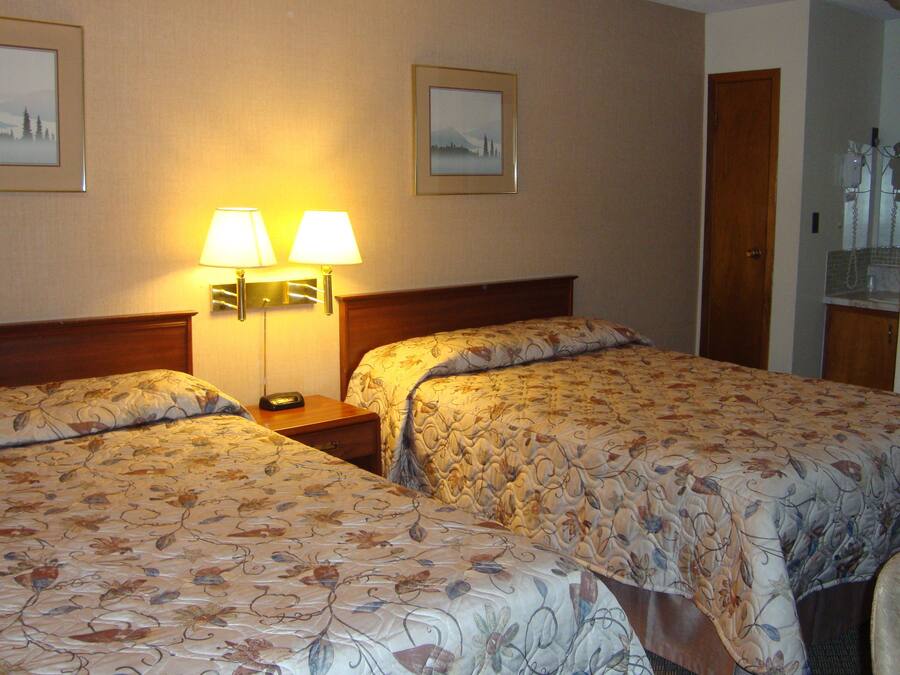 A hotel room with two beds, a nightstand with lamps, and framed pictures on the wall.