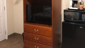 Habitación de hotel con tocador de madera, televisor, microondas y cafetera.