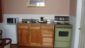 Una cocina compacta con armarios de madera, microondas, cafetera y estufa antigua.