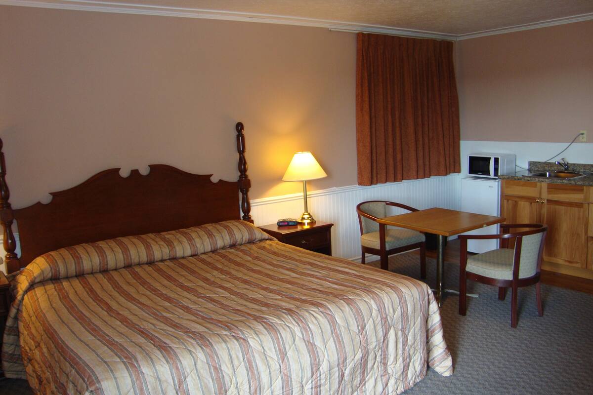 Quarto de hotel com cama, escrivaninha, cadeira, luminária, micro-ondas e armário.