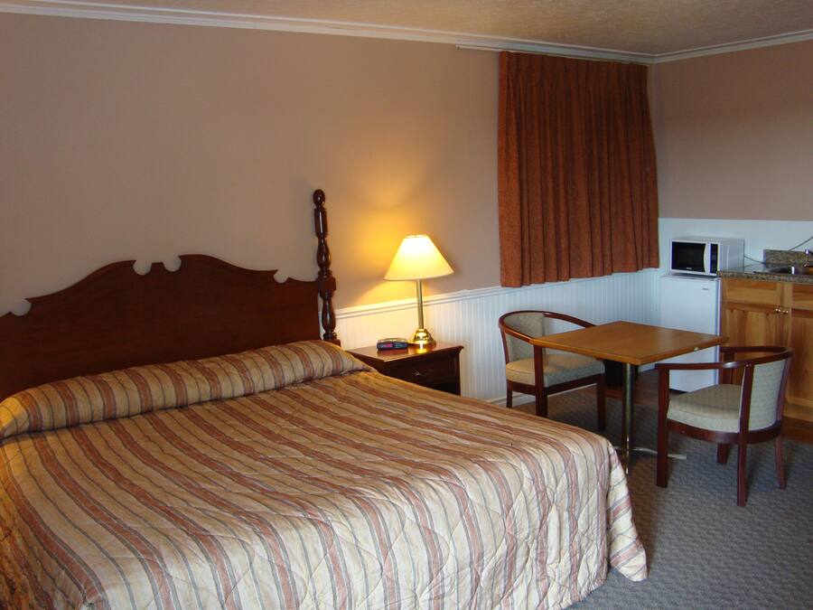 A hotel room with a bed, a desk, a chair, a lamp, a microwave, and a cabinet.