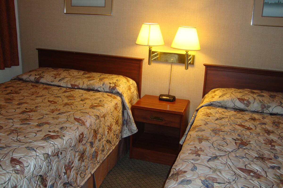 Quarto de hotel com duas camas, cada uma com roupa de cama estampada com flores, uma mesinha de cabeceira com abajur e um espelho.