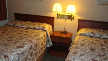 Habitación de hotel con dos camas, cada una con ropa de cama de motivos florales, una mesita de noche con lámpara y un espejo.