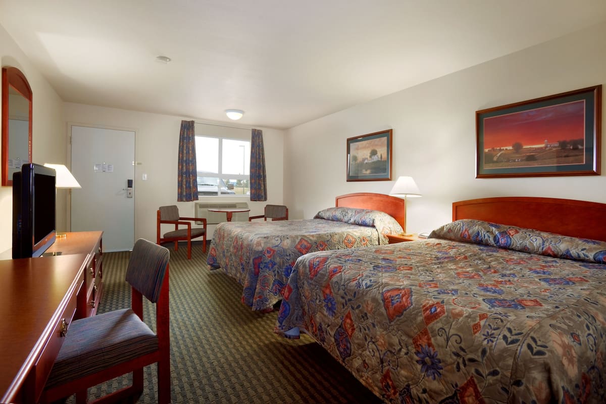Une chambre d’hôtel avec deux lits, un bureau, une chaise, une télévision et une fenêtre avec des rideaux.