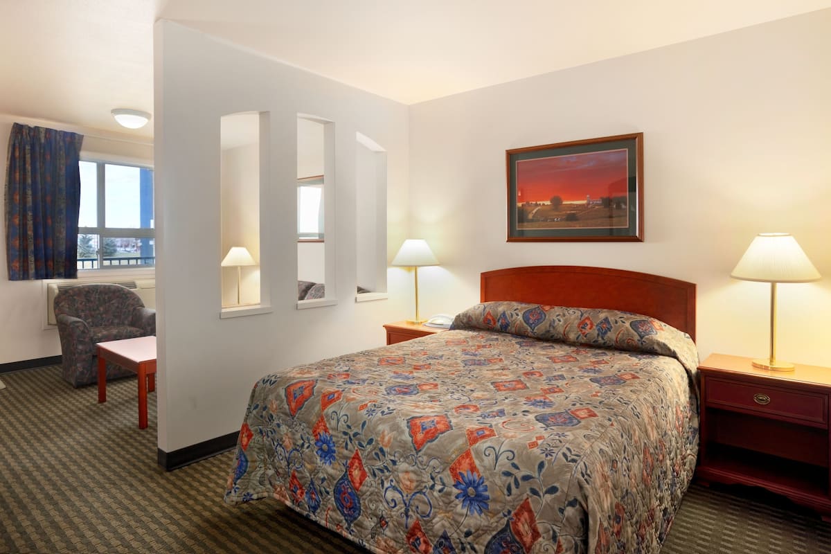 Une chambre d’hôtel avec un grand lit, deux tables de chevet avec des lampes, une chaise, un bureau et une fenêtre avec des rideaux.