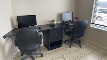 A modern office space with a black desk, two black office chairs, a computer monitor, a keyboard, and a mouse.