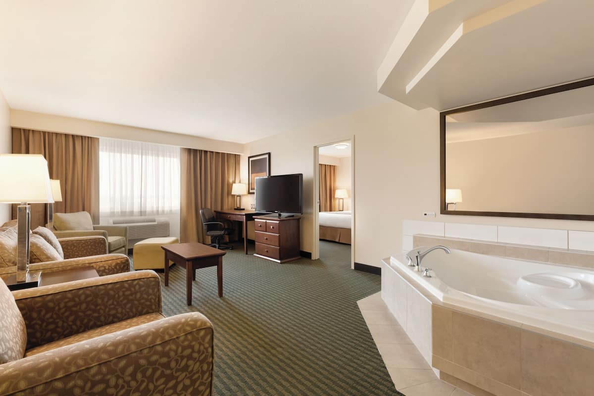 Une chambre d’hôtel équipée d’un canapé, d’un bureau, d’une télévision et d’une salle de bain avec baignoire, ainsi que d’un grand miroir.