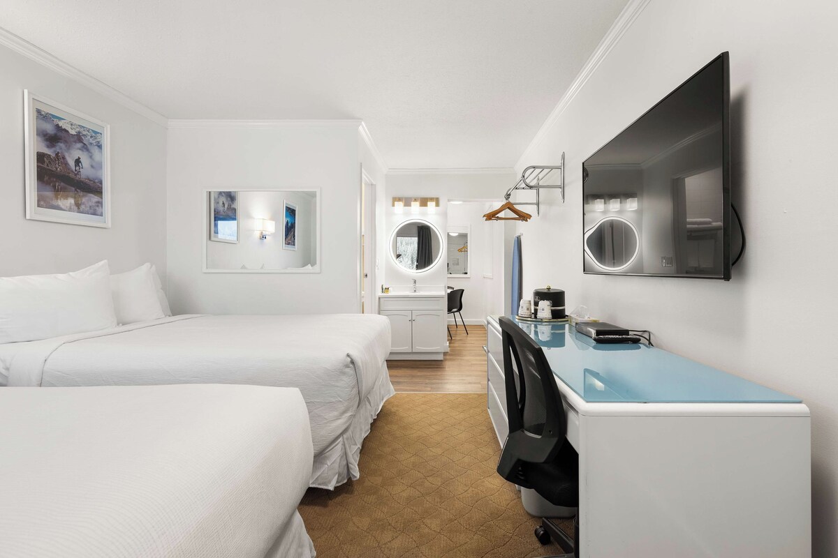 Une chambre d’hôtel avec deux lits, un bureau avec un ordinateur, un miroir et un téléviseur fixé au mur.