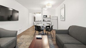 Een moderne woonkamer met een grijze bank, een fauteuil met een patroon, een houten salontafel, en een eethoek met een ronde tafel en stoelen.