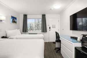 Habitación de hotel con dos camas, un escritorio, una silla, un televisor y una ventana con cortinas.