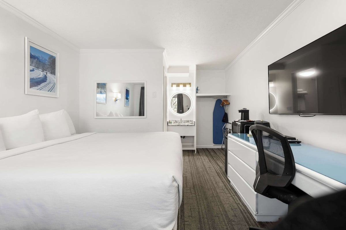 Ett hotellrum med en stor säng, ett skrivbord med en stol, en TV, en spegel och en garderob.