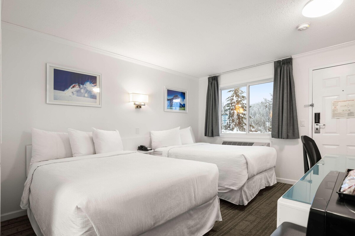Een hotelkamer met twee bedden, een bureau, een stoel, een raam met gordijnen en wandlampen.