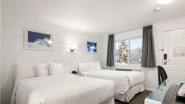 Een hotelkamer met twee bedden, een bureau en een raam met gordijnen.