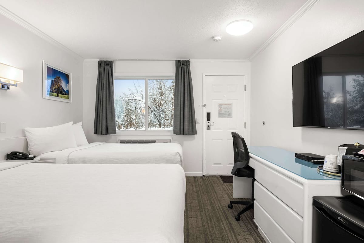 Ett hotellrum med två sängar, ett skrivbord, en stol, en tv och ett fönster med gardiner.