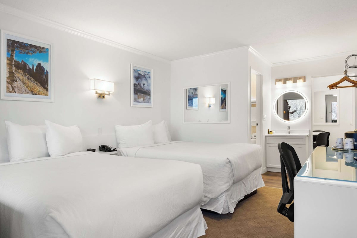 Two single beds with white bedding, a desk, and a round mirror.