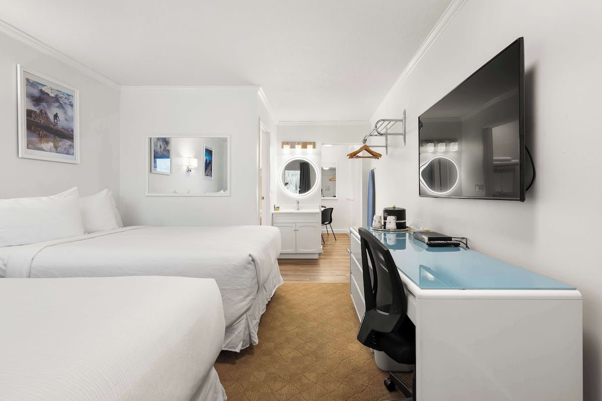 Ett hotellrum med två sängar, ett skrivbord med en dator, en spegel och en TV som är monterad på väggen.