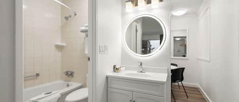 A modern bathroom with a bathtub, toilet, vanity with a mirror, and a shower.