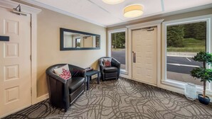 Een hotellobby met een vloerbedekt met tapijt, twee zwarte leren fauteuils, een kleine tafel, een spiegel en een groot raam met uitzicht op de straat.